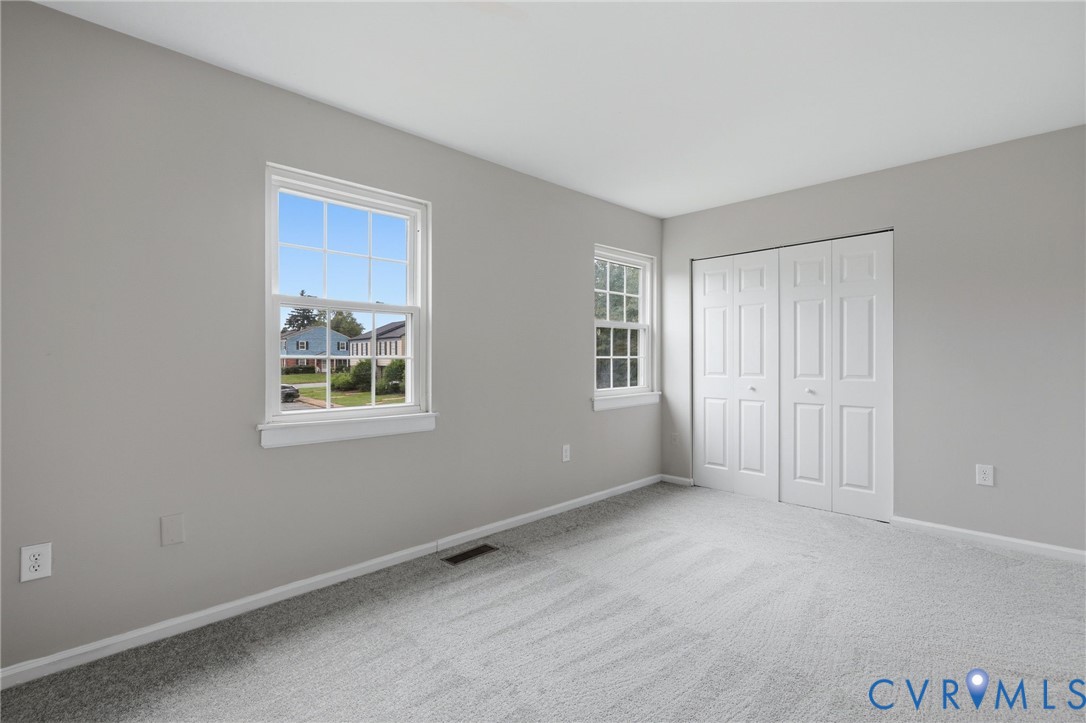 Neutral gray wall paint with white trim, light gray patterned carpeting, double-pane windows, and a bi-fold closet door
