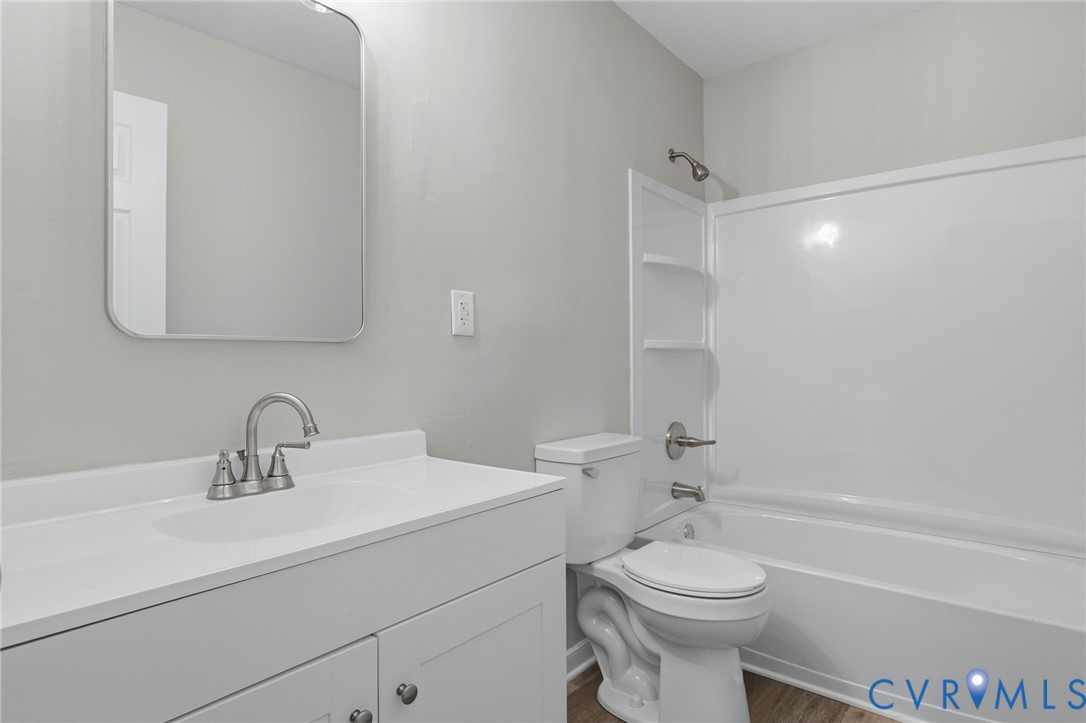 Bathroom featuring a white vanity with integrated sink, brushed nickel faucet, framed mirror, and a white tub/shower combination with built-in shelving