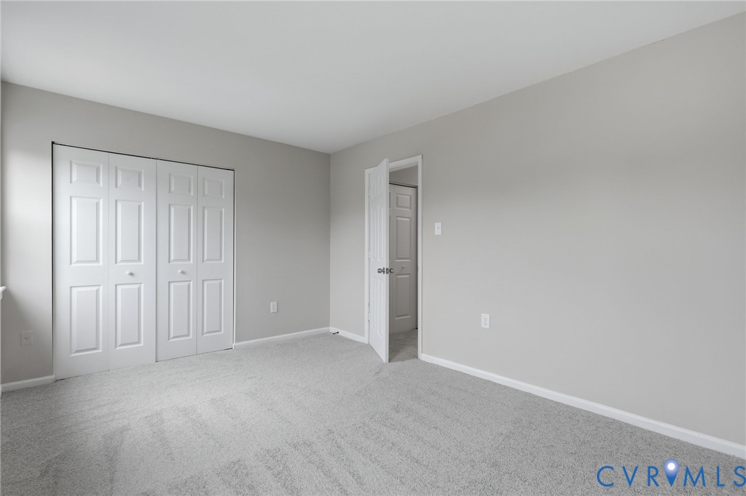 Spacious room featuring light gray carpeting, neutral wall paint, white baseboards, and a white bi-fold closet