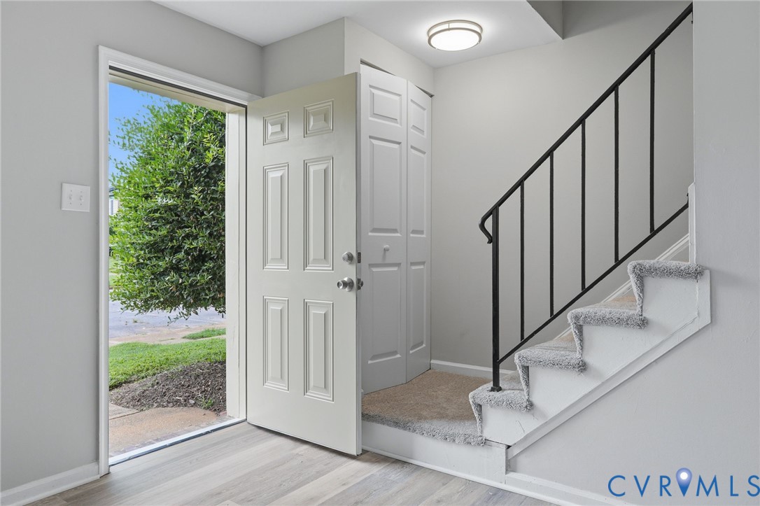 Entryway featuring wood-finish flooring, a white paneled door, and a staircase with carpeted treads and a black metal handrail
