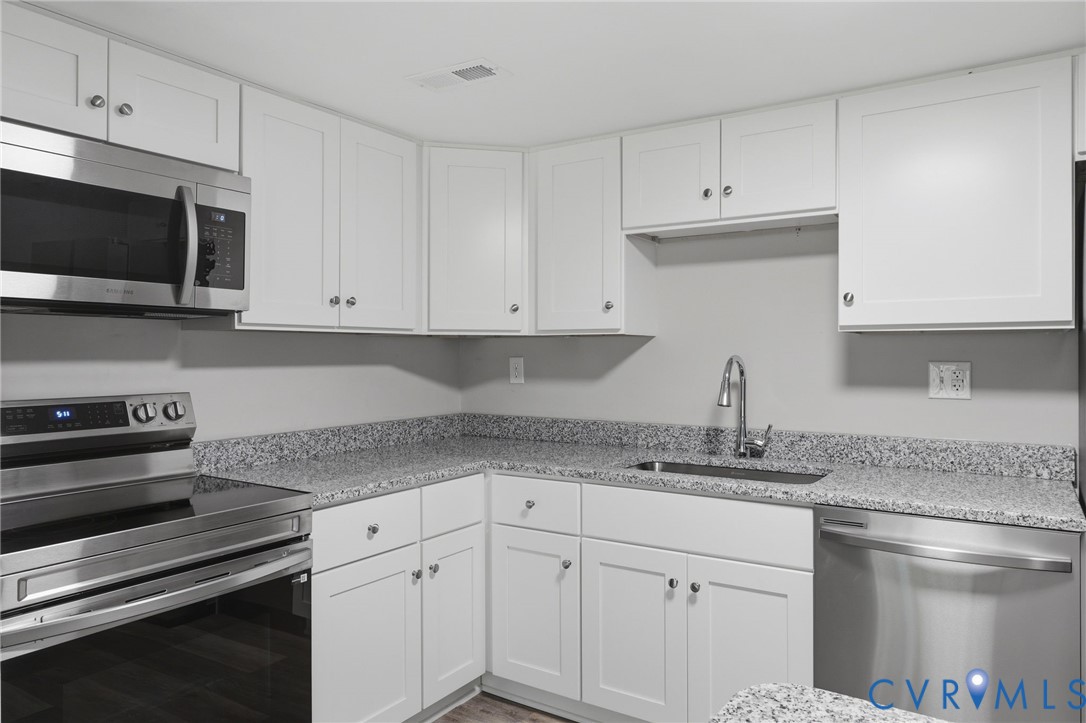 Kitchen featuring white shaker-style cabinetry, a stainless steel appliance suite, speckled countertops, a double basin sink with a gooseneck faucet, and wood-finish flooring