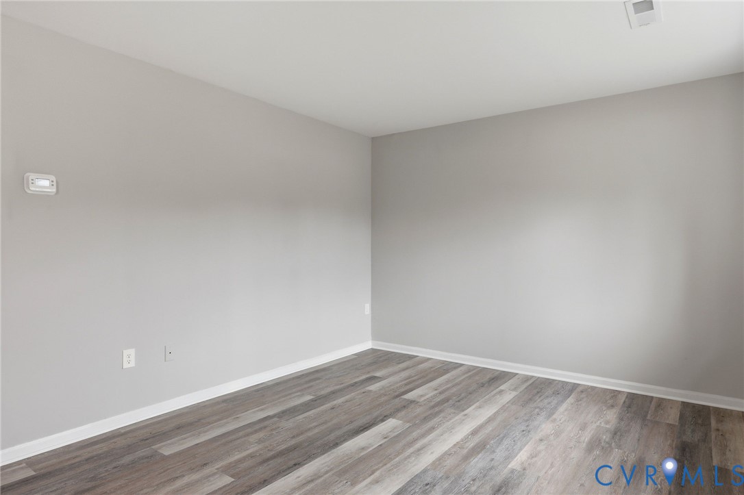 Spacious room featuring wood-finish flooring, light grey painted walls, white baseboards, and a ceiling-mounted HVAC vent