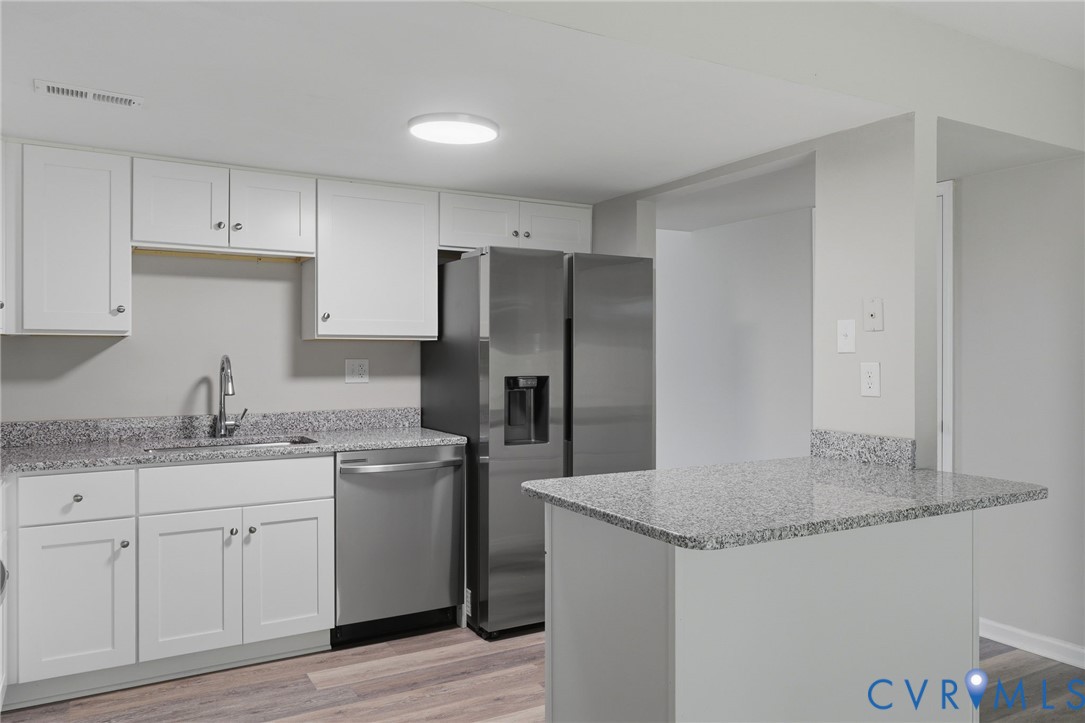 Kitchen featuring white cabinetry, speckled countertops, stainless steel appliances, and wood-finish flooring