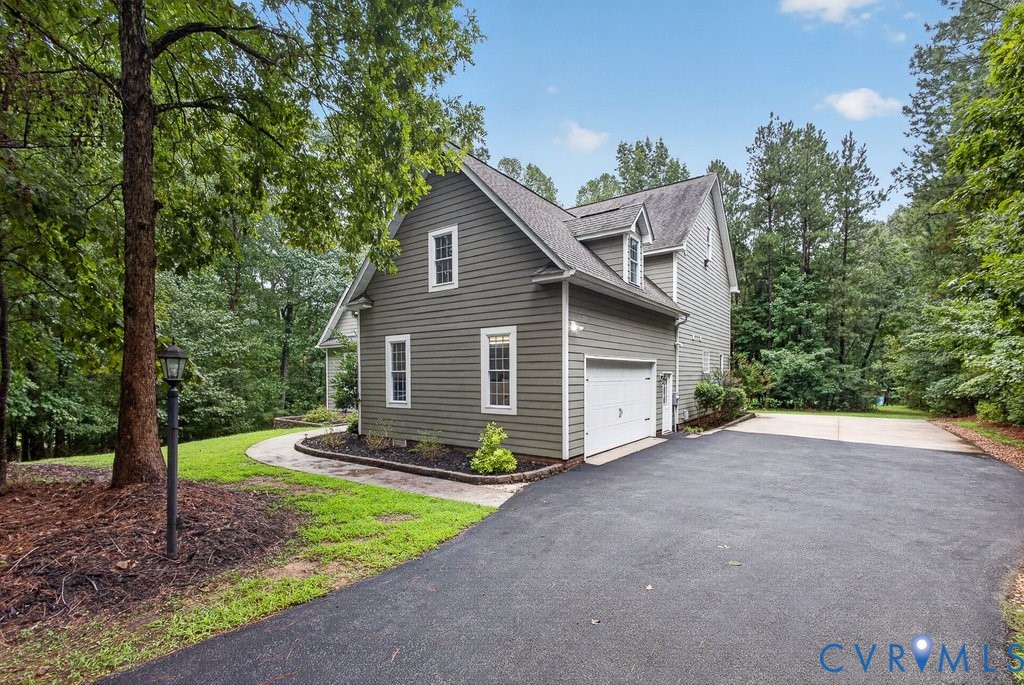 Two-story exterior with dormer windows, attached garage, paved driveway, and established landscaping