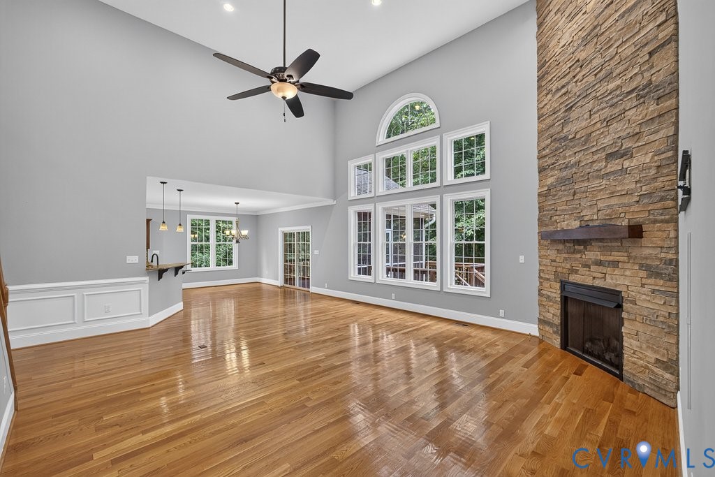 Vaulted ceilings with recessed lighting, hardwood flooring, stacked stone fireplace with wood mantel, multiple windows with transom, and panel molding