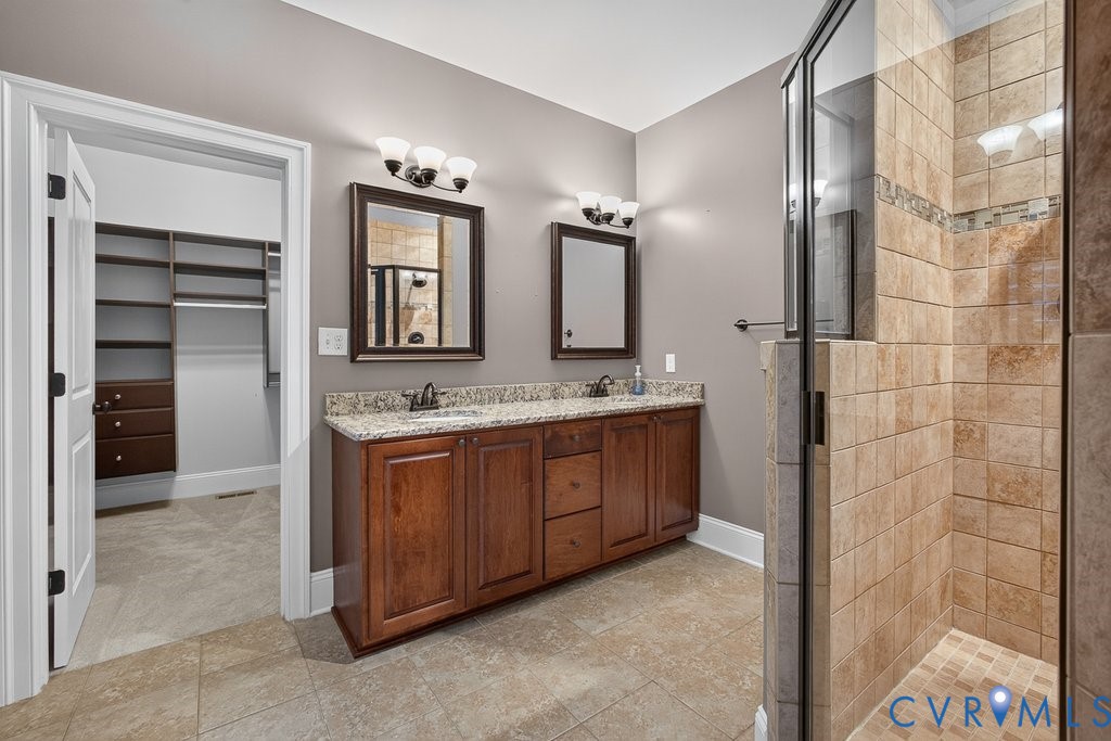 Spa-inspired primary bathroom featuring a dual-sink vanity with wood cabinetry, granite countertop, and polished nickel fixtures