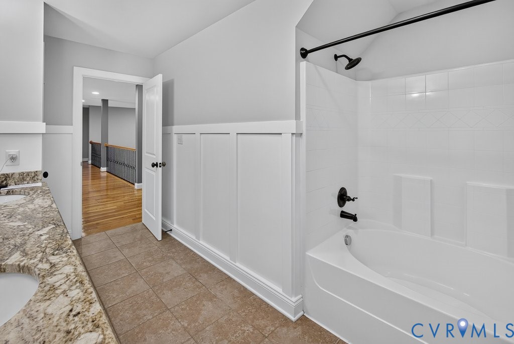 Dual vanity with stone countertop, tile flooring, board and batten wall detailing, and a tub/shower combination with matte black fixtures