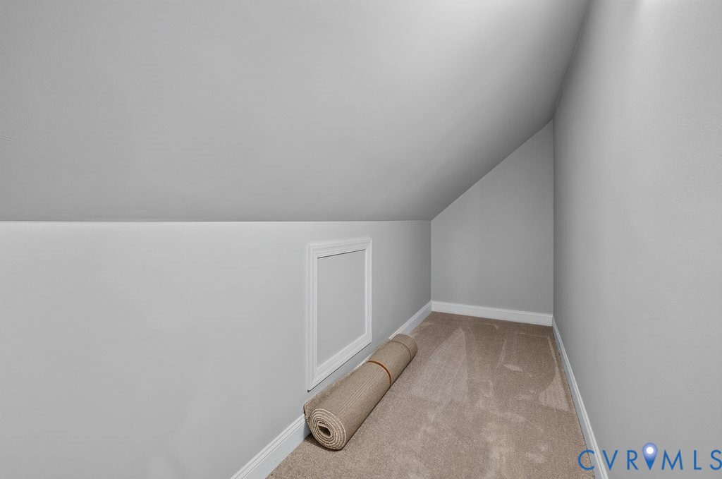 Sloped ceiling with light gray painted walls, a white trim access panel, and neutral-toned carpet flooring
