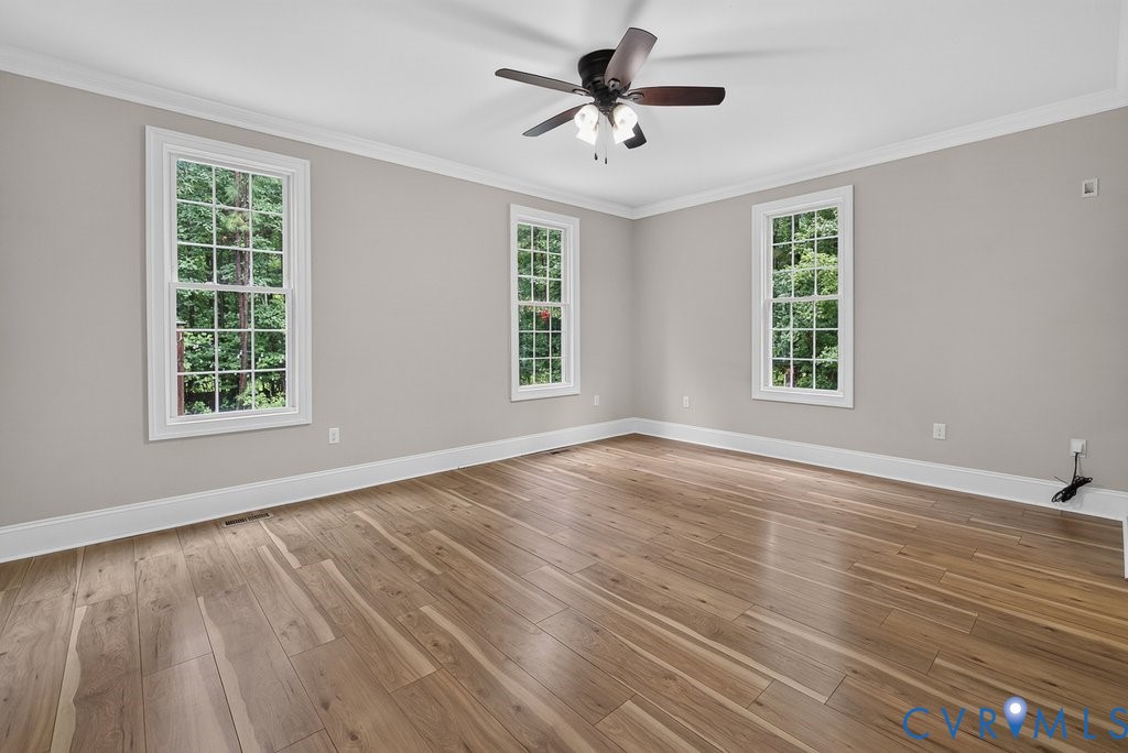 Wood-finish flooring, three double-hung windows, crown molding, and a ceiling fan with integrated lighting