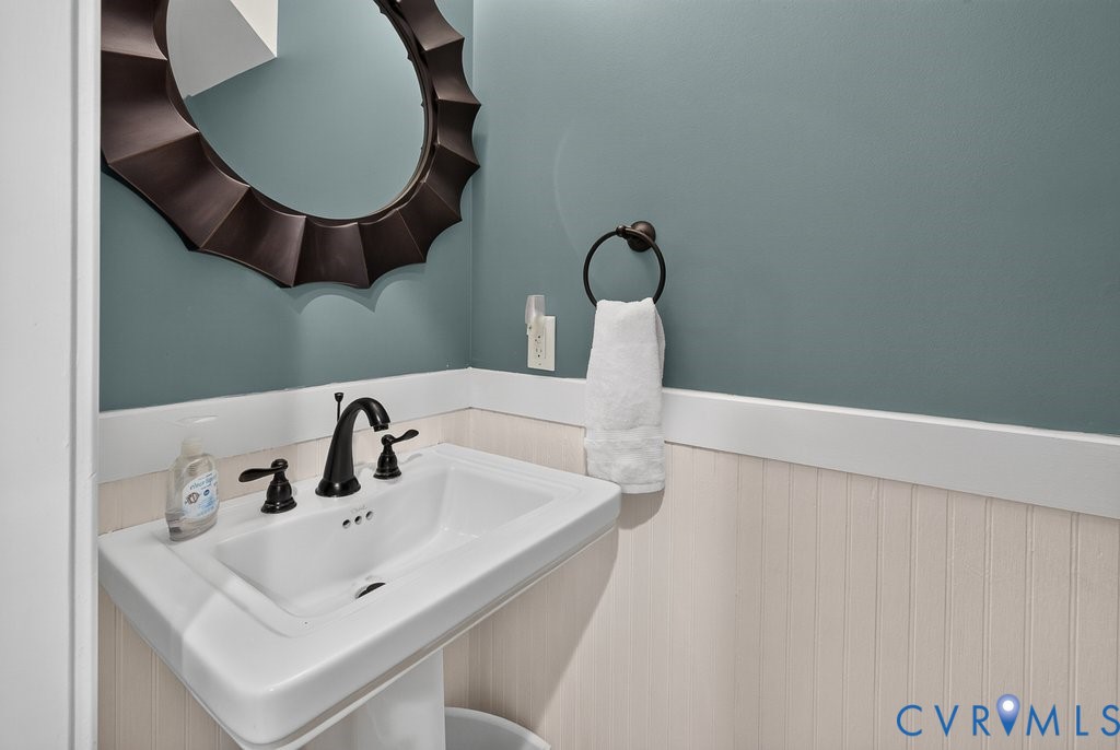 Pedestal sink with dark bronze faucet, beadboard wainscoting, and a decorative mirror