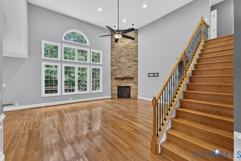 Vaulted ceiling with recessed lighting, wood-finish flooring, stone-clad fireplace, and a full-light window wall with an arched transom