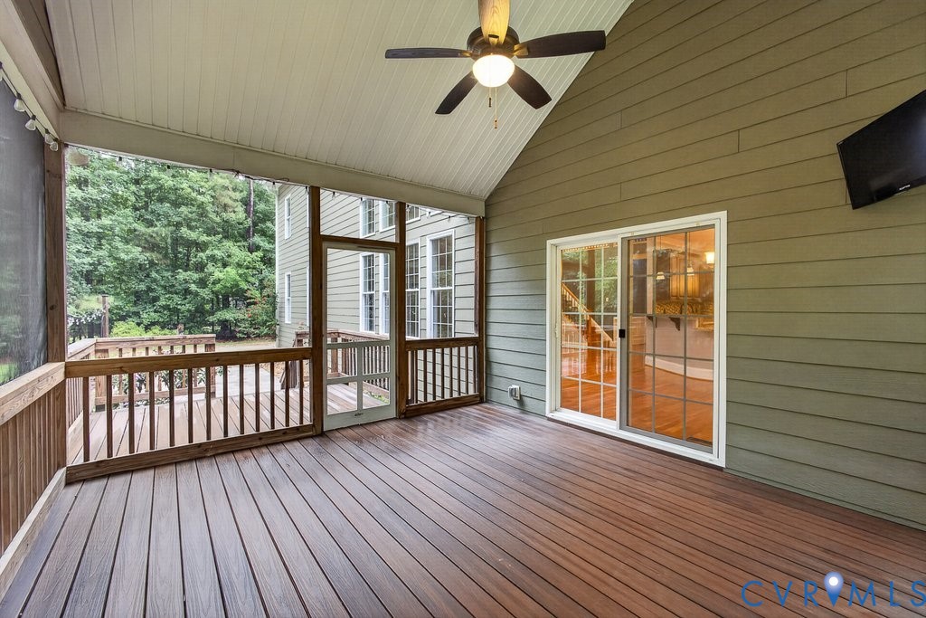 Screened porch featuring a vaulted ceiling, ceiling fan, and composite decking