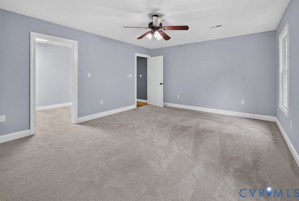 Spacious room with light gray carpeting, neutral wall color, white trim, a ceiling fan, and a large window