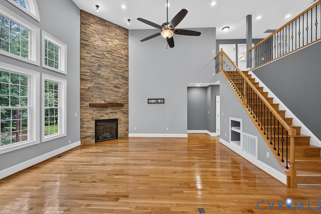 Hardwood flooring throughout, a stacked stone fireplace with a wood-finish mantel, and a two-story ceiling