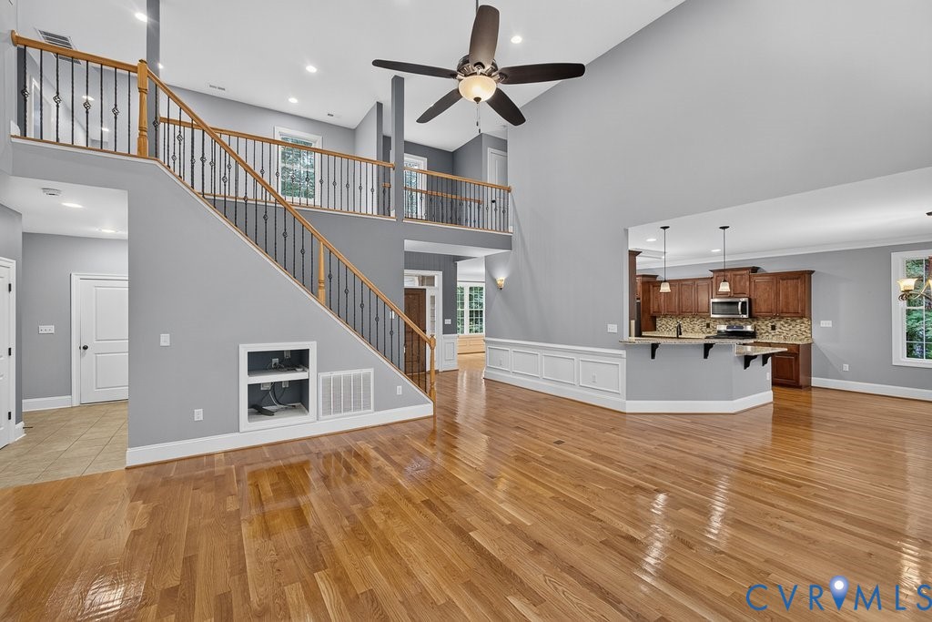 Vaulted ceiling with a ceiling fan, wood-finish flooring, staircase with wood handrails and wrought iron balusters, interior balcony, and a kitchen island with pendant lighting