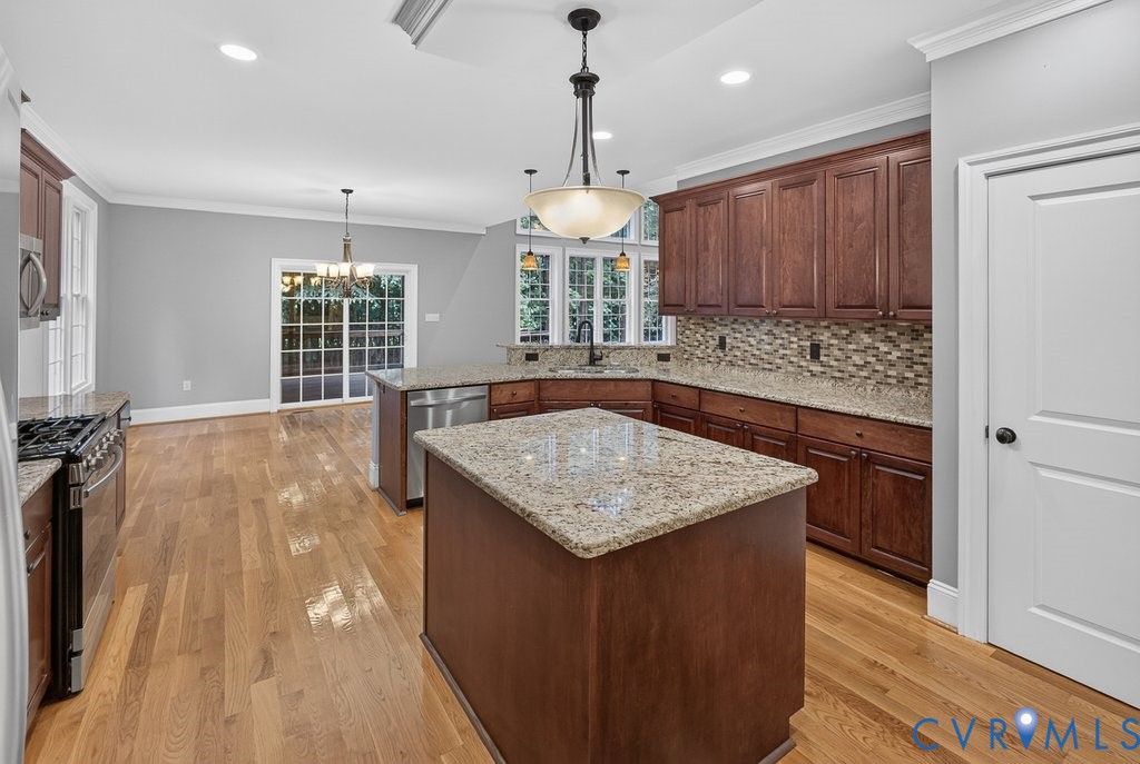 Hardwood flooring, two-tier kitchen island, stainless steel appliances, granite countertops, and mosaic tile backsplash