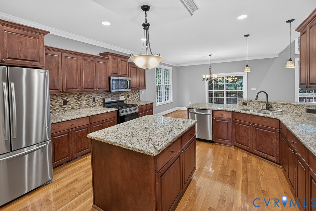 Kitchen with wood-finish flooring, central island, stainless steel appliances, granite countertops, and wood cabinetry