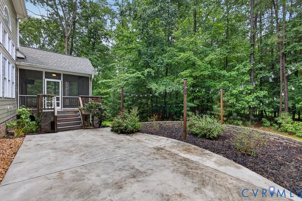 Concrete patio with a screened porch, exterior steps, and a landscaped retaining wall