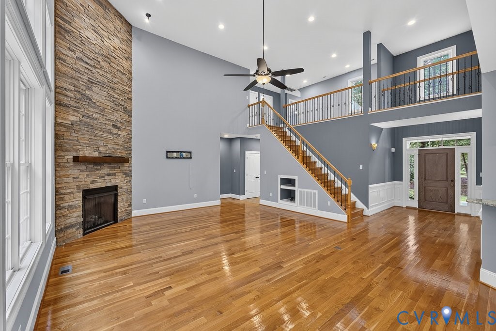 Hardwood flooring throughout, two-story stone fireplace with wood mantel, vaulted ceilings, open-tread staircase with wood handrails, and a second-story balcony