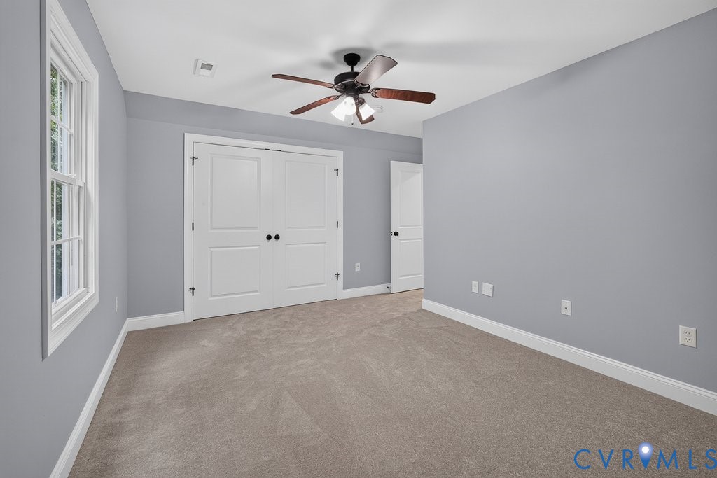 Wall-to-wall carpeting, white trim, double bi-fold doors, white window framing, and an overhead ceiling fan