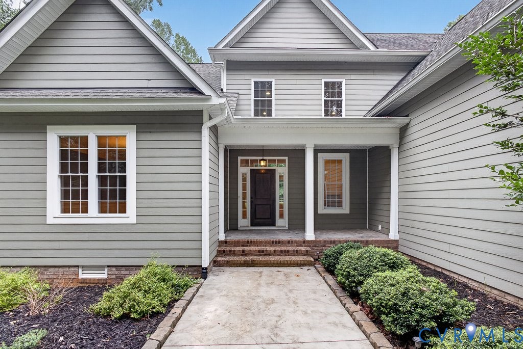 Exterior featuring gray horizontal siding, an inviting covered entry with white columns, brick steps, and a concrete pathway