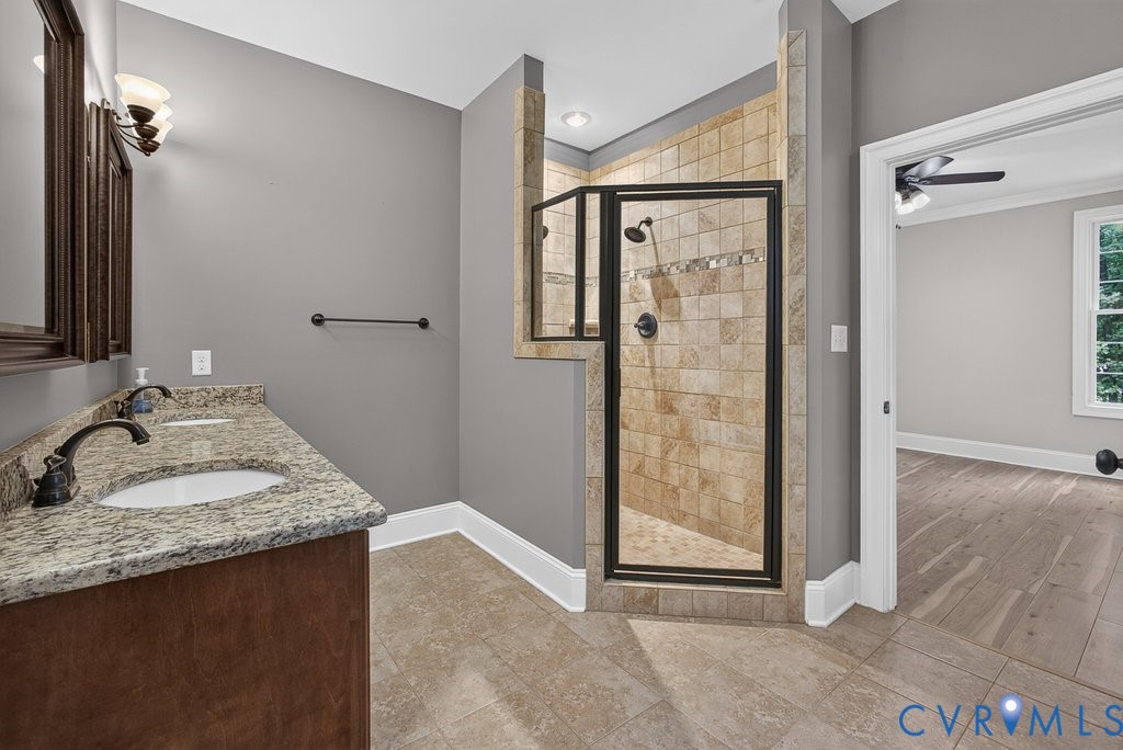 Dual vanity with stone countertop, tile flooring, and a tiled shower with glass enclosure