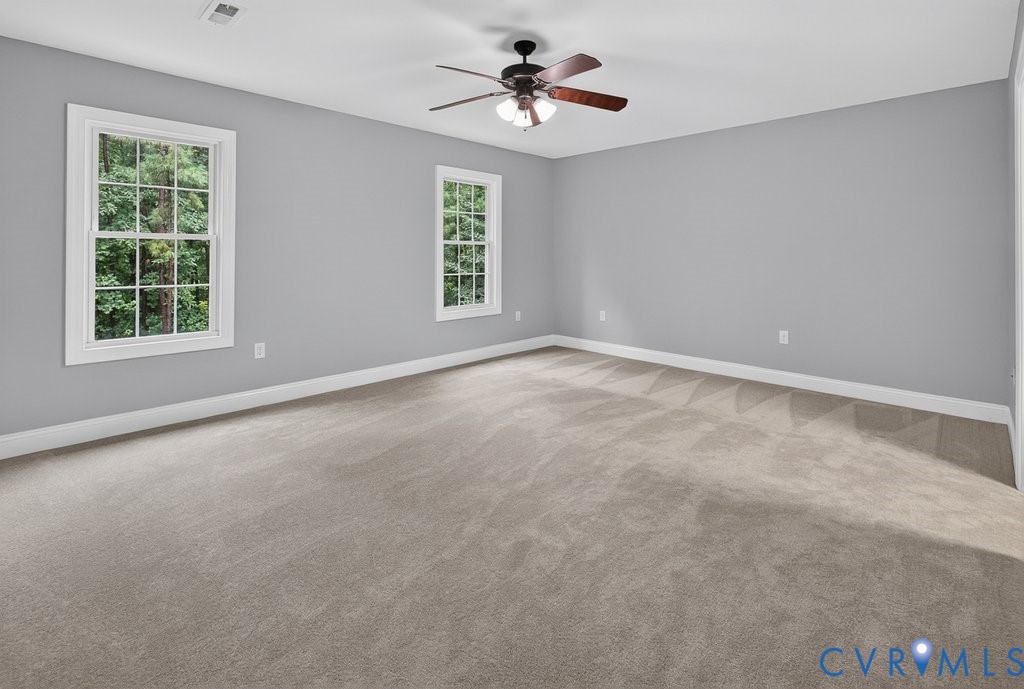 Spacious room featuring neutral carpeting, two double-hung windows with white trim, and a ceiling fan with integrated lighting