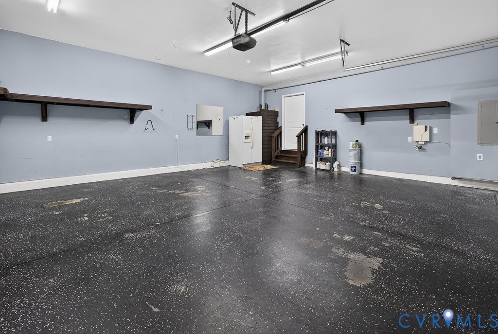 Spacious garage with light blue walls, built-in wooden shelving, and a painted concrete floor