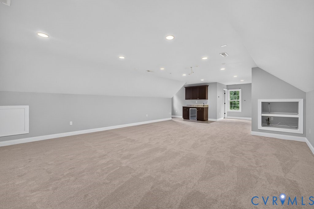 Recessed lighting, sloped ceilings, built-in wet bar with dark wood cabinetry, built-in beverage refrigerator, and built-in shelving