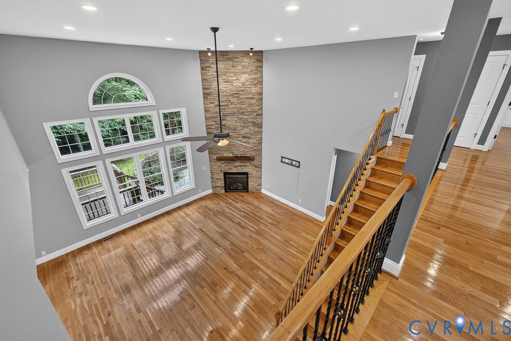 Vaulted ceiling with an arched window, stacked stone fireplace, wood-finish flooring, and a ceiling fan