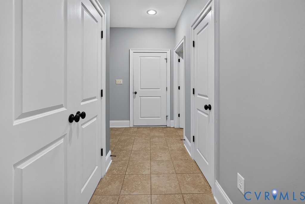 Bright hallway with crisp white six-panel doors, black hardware, and warm tile flooring throughout