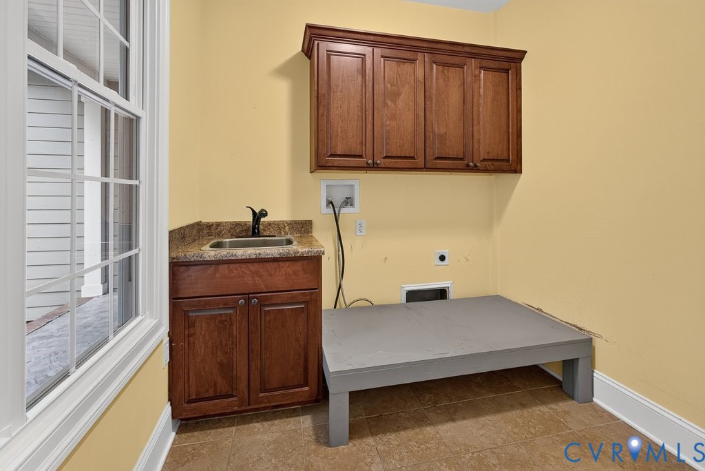 Utility room featuring a window, built-in cabinetry, a sink with a dark faucet, a countertop, and tile flooring