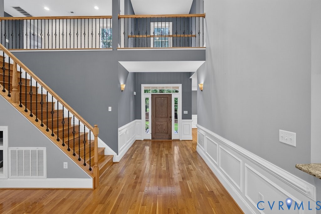Hardwood flooring throughout, two-story foyer, elegant wainscoting, solid wood entry door, and decorative wrought iron balusters