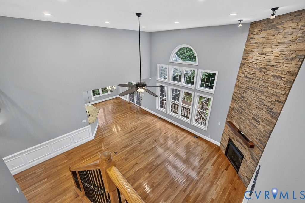 Two-story living area featuring wood-finish flooring, a stone-clad fireplace with a wood mantle, a multi-pane window array, and a ceiling fan