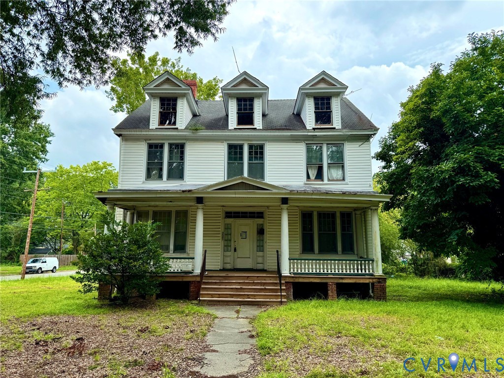Two-story residence featuring a covered front porch with columnar supports and a balustrade, multiple dormer windows on the roofline, and a symmetrical facade