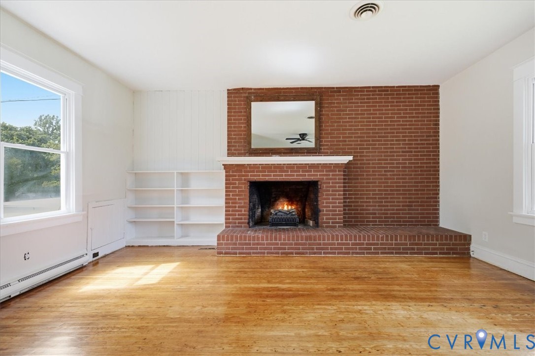 Brick fireplace with a white mantel, wood-finish flooring, and built-in shelving