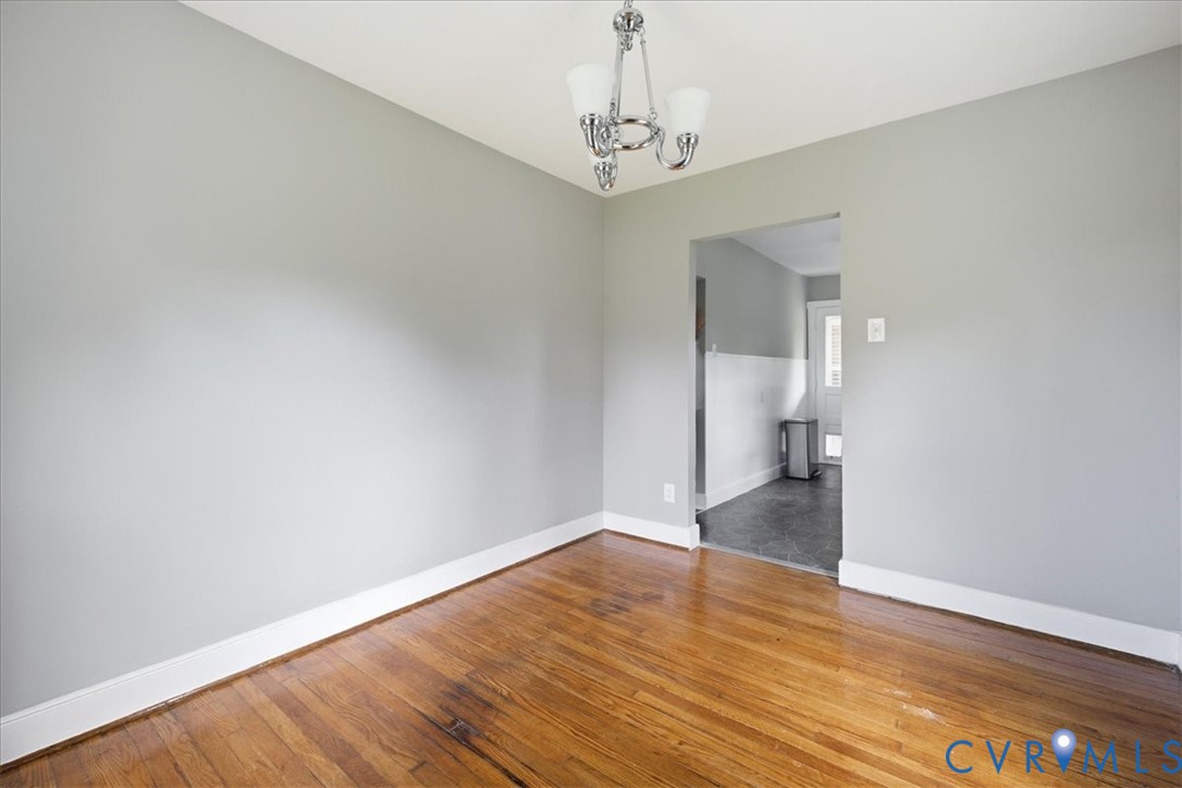 Wood-finish flooring with white trim, light gray walls, and a ceiling-mounted chandelier