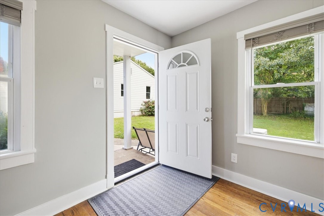 White paneled front door with an arched transom, wood-finish flooring, and light gray walls