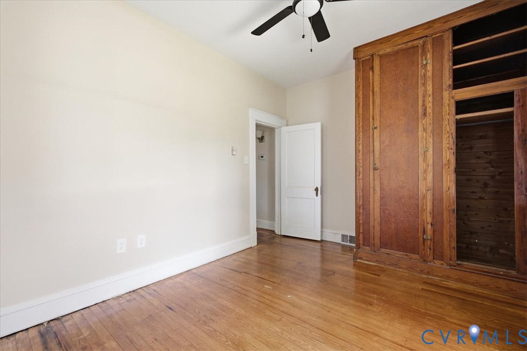 Spacious bedroom featuring hardwood flooring, ceiling fan with integrated lighting, and custom wood-finish built-in cabinetry