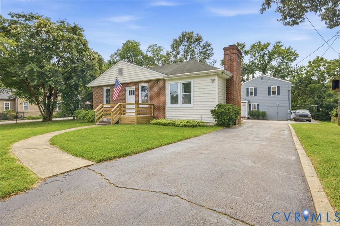 Brick and siding exterior with a prominent brick chimney, featuring a front porch with wood railing and steps, a paved driveway, and a concrete pathway Brick and siding exterior with a prominent brick chimney, featuring a front porch with wood railing and steps, a paved driveway, and a concrete pathway