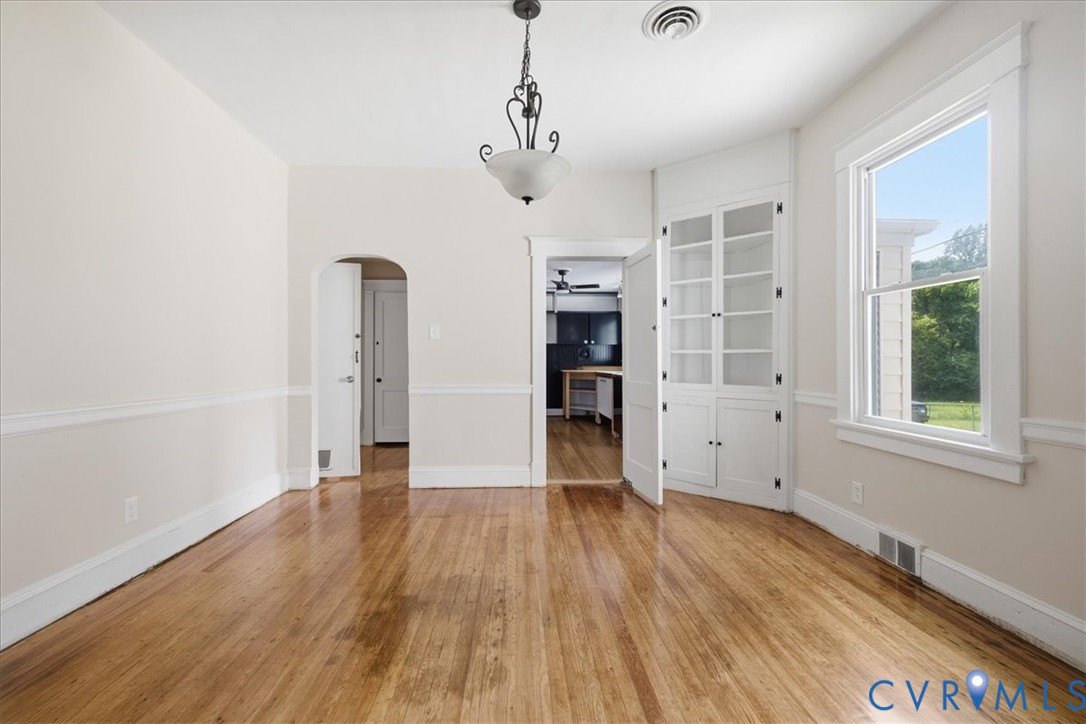 Hardwood flooring, crown molding, built-in cabinetry, arched doorway, and a ceiling-mounted light fixture