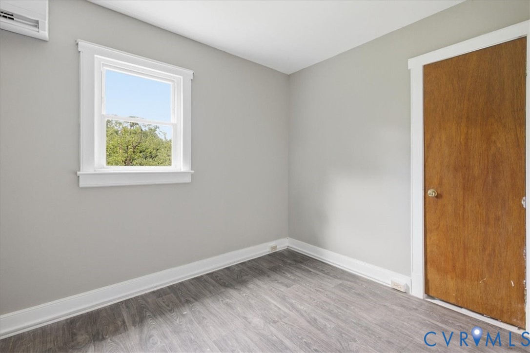 Gray-toned walls with wood-finish flooring, white window trim, and a split air conditioning unit
