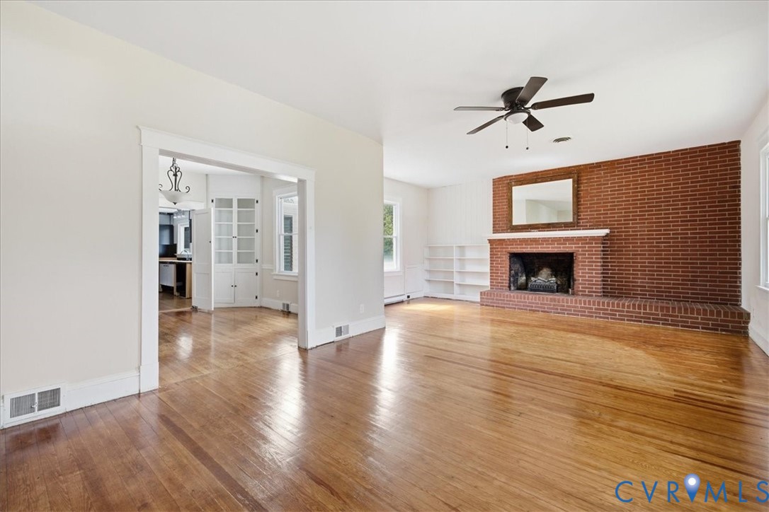 Hardwood flooring, brick fireplace with mantel, built-in shelving, ceiling fan, and cased opening