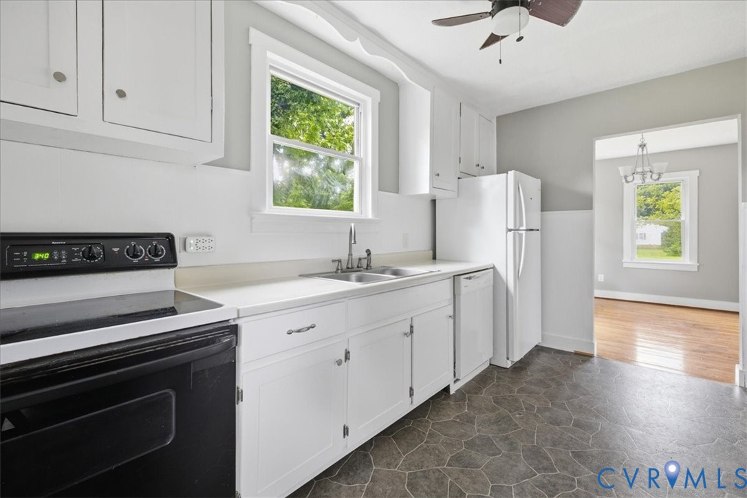 Kitchen featuring white cabinetry, a double basin stainless steel sink, black range, and stone-patterned flooring