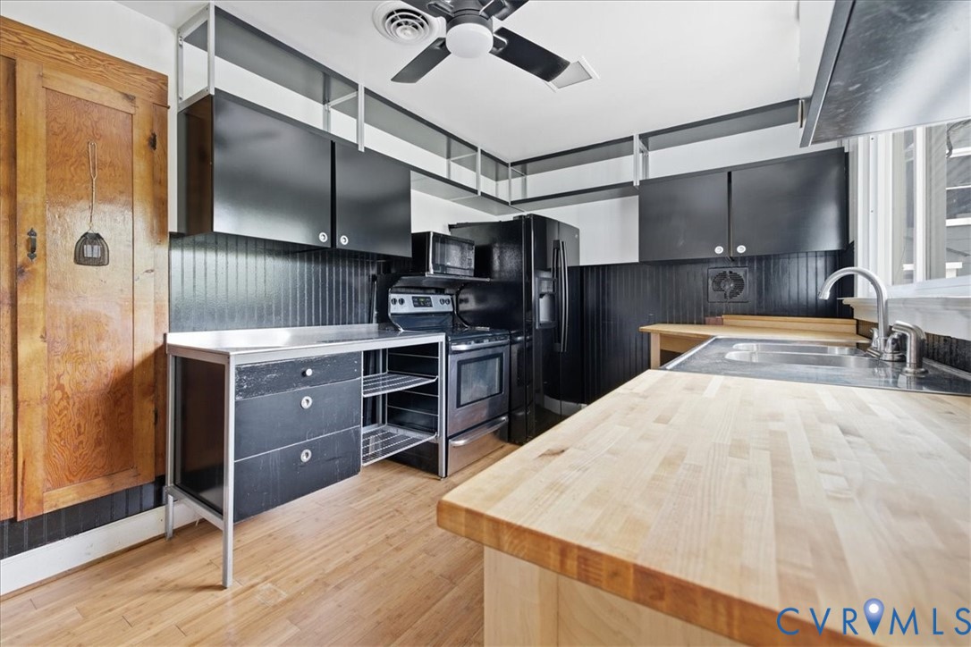Wood-finish flooring with solid wood countertops, black cabinetry, and stainless steel sink