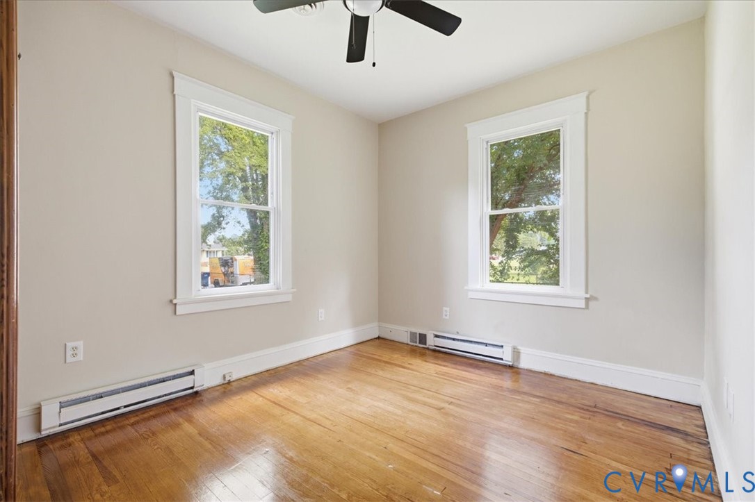 Hardwood flooring, painted walls, two windows with white trim, and a ceiling fan