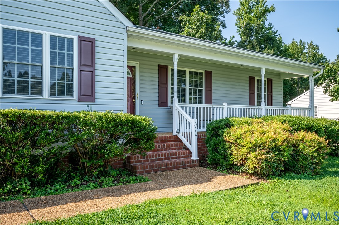 Charming farmhouse-style residence featuring light blue horizontal siding, brick foundation, and a welcoming front porch with white railings and columns Charming farmhouse-style residence featuring light blue horizontal siding, brick foundation, and a welcoming front porch with white railings and columns