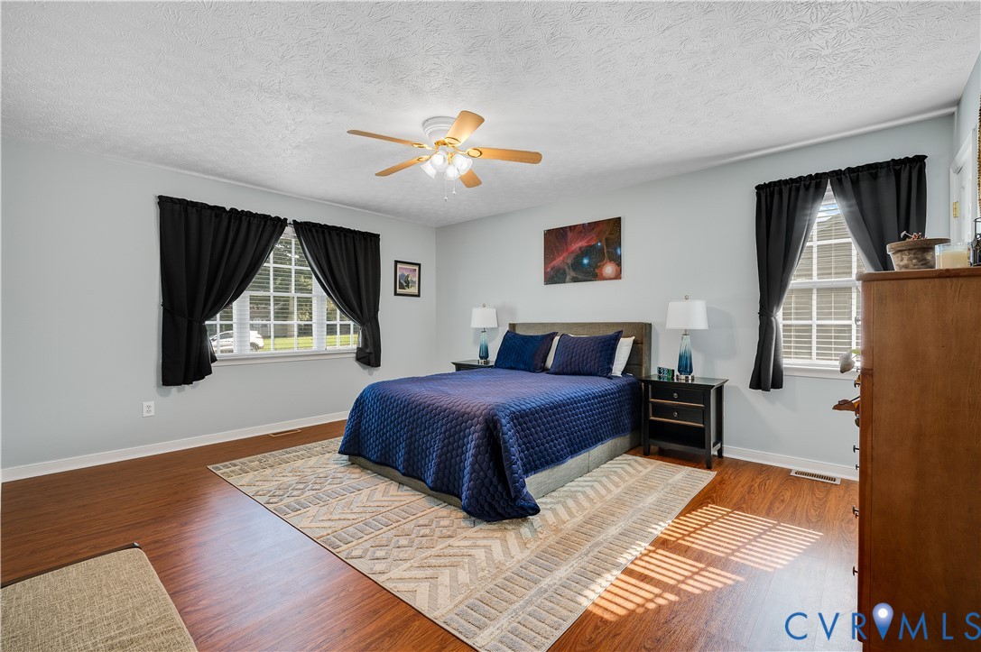Spacious primary bedroom featuring hardwood flooring, a ceiling fan with integrated lighting, and abundant natural light from multiple windows.