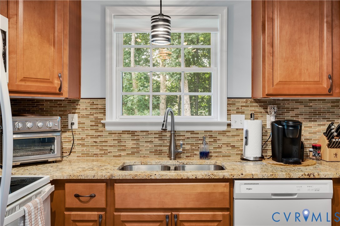 Kitchen featuring wood cabinetry, granite countertops backsplash, a double basin sink with a gooseneck faucet, and a built-in dishwasher
