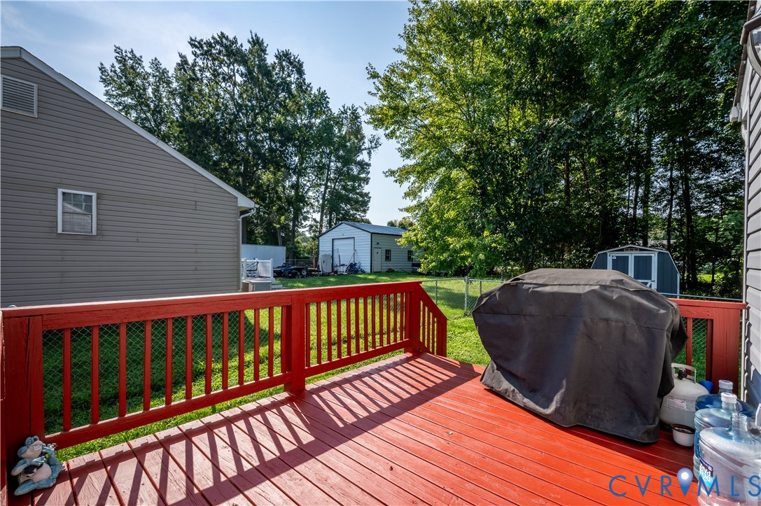 Expansive red-stained deck with baluster railing, leading to a fenced yard with mature trees